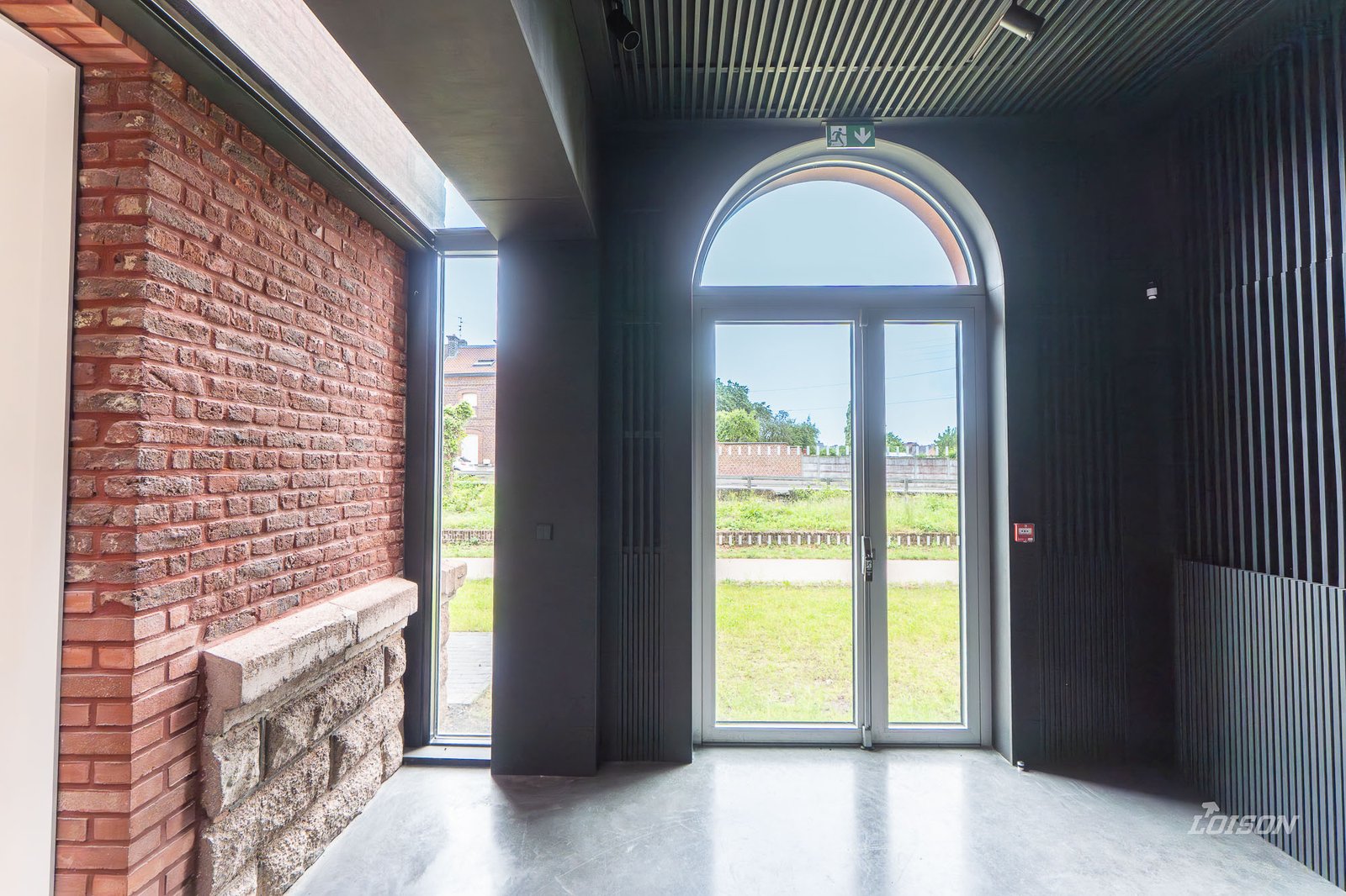 Réhabilitation de l’Ancienne Gare des Houillères – Fresnes-sur-Escaut Dans l'extension, la porte aluminium cintrée et le mur-rideau de liaison contre le pignon en briques