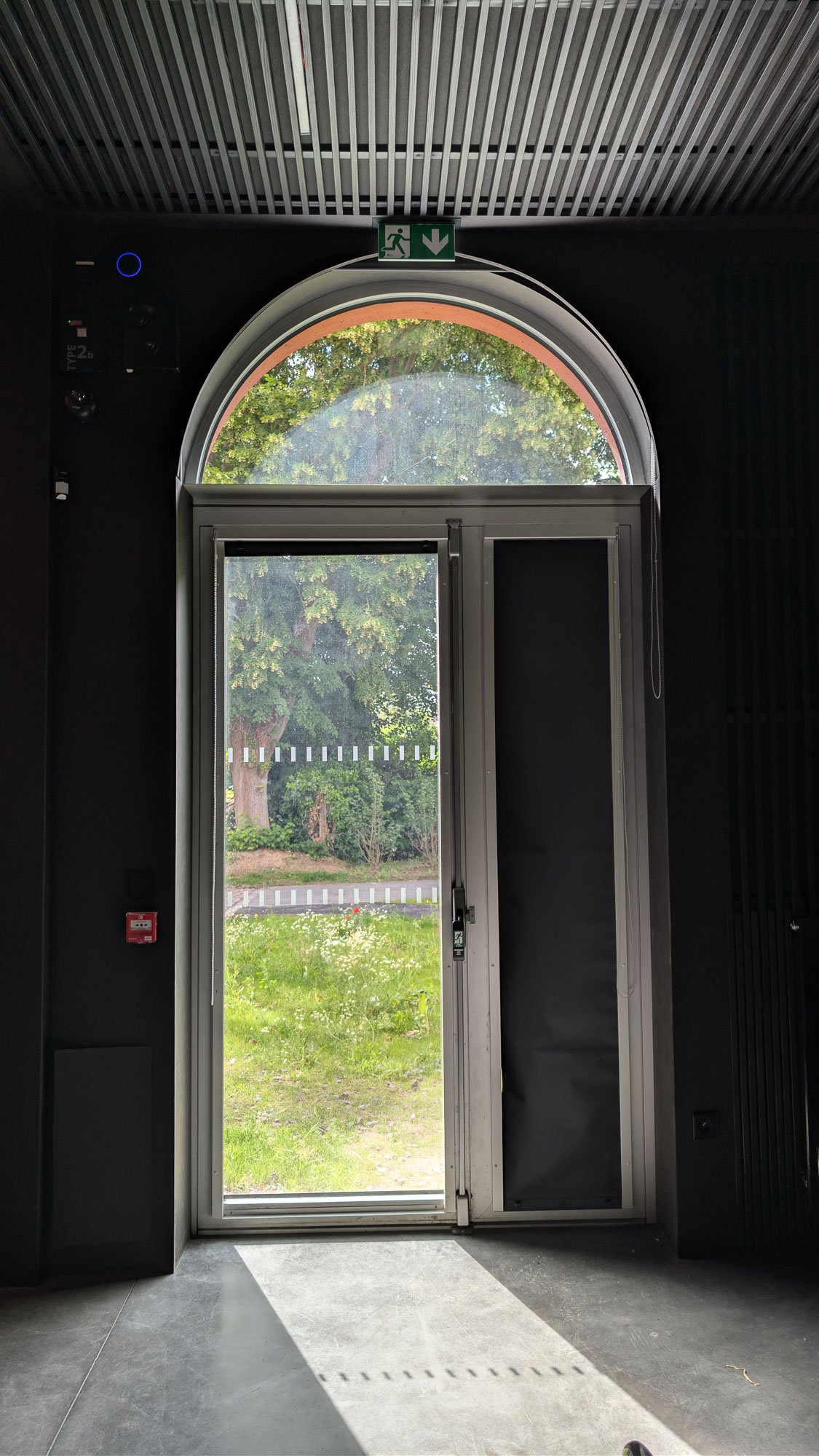 Réhabilitation de l’Ancienne Gare des Houillères – Fresnes-sur-Escaut Une porte aluminium à deux vantaux sous imposte cintrée, avec son store intérieur