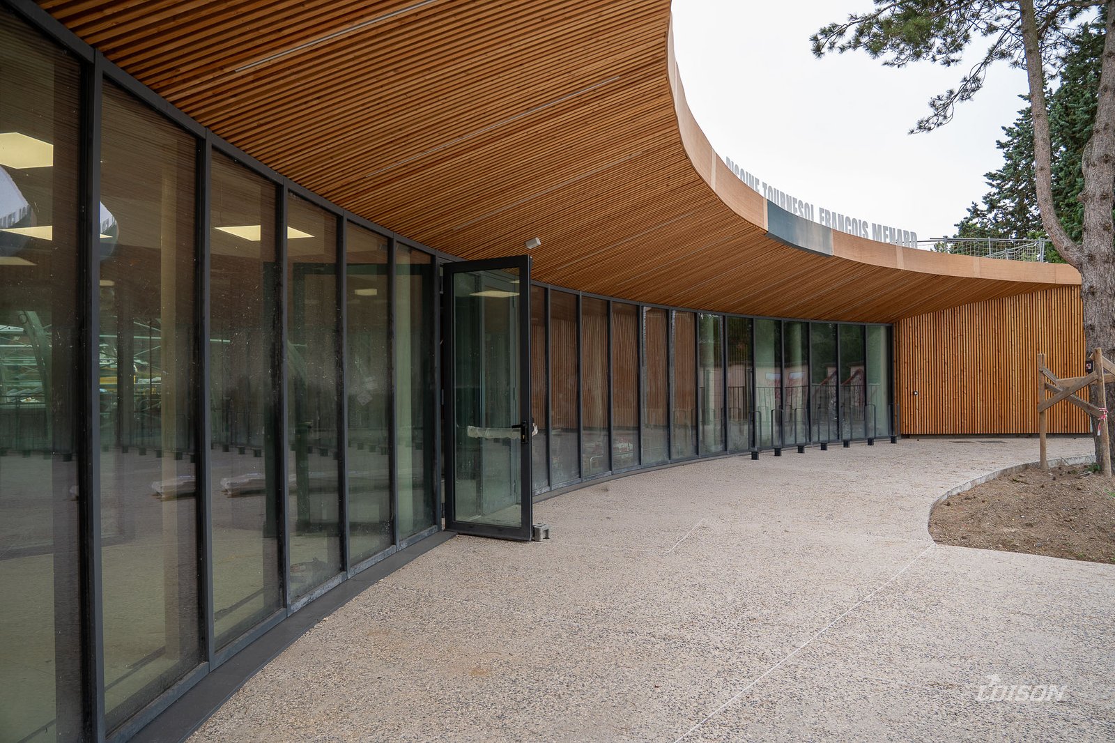 L'entrée de la piscine Tournesol François Ménard, son mur-rideau courbe et son avancée en bois