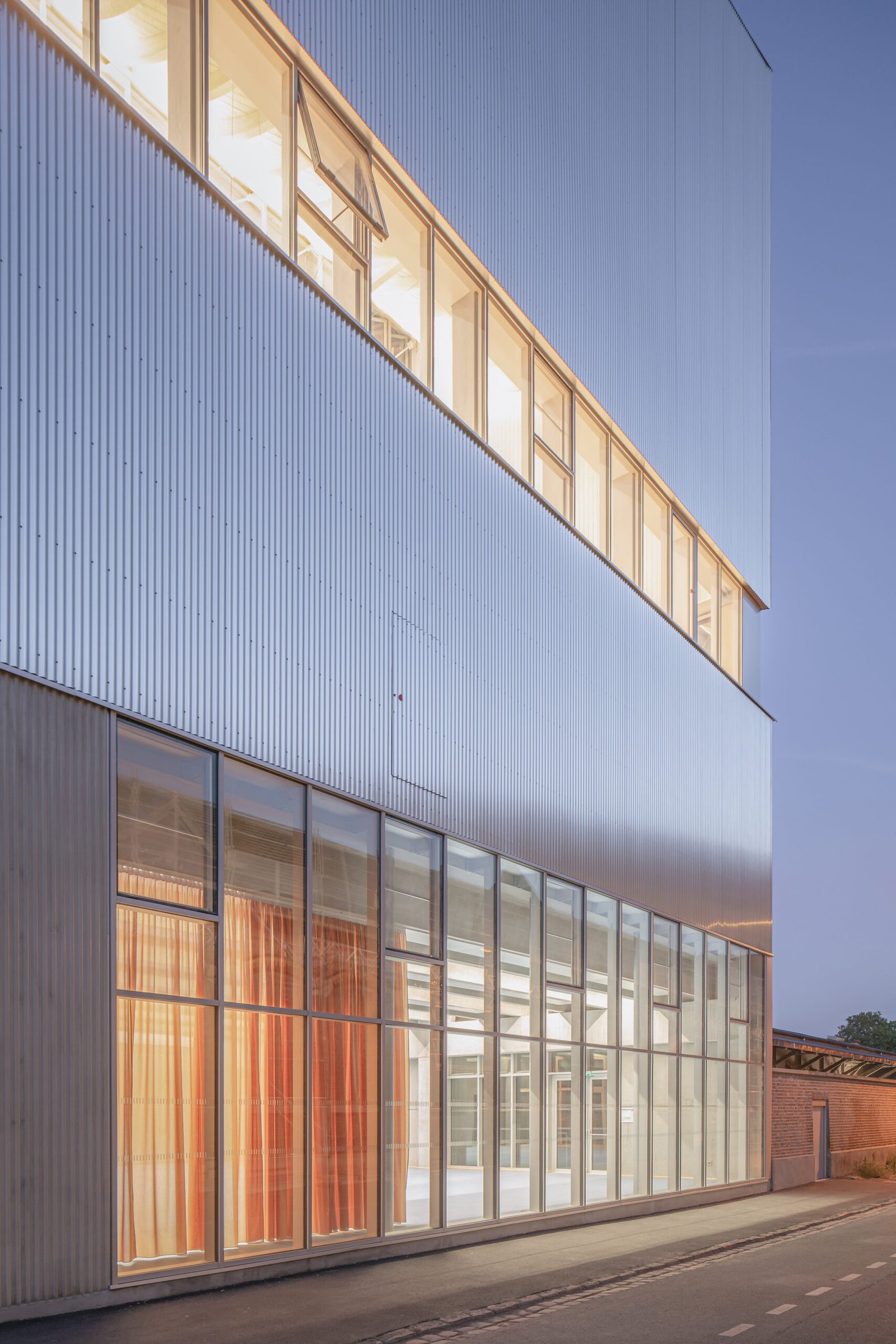 La façade en aluminium ondulé et le bandeau vitré de la salle de basket, à la tombée du jour