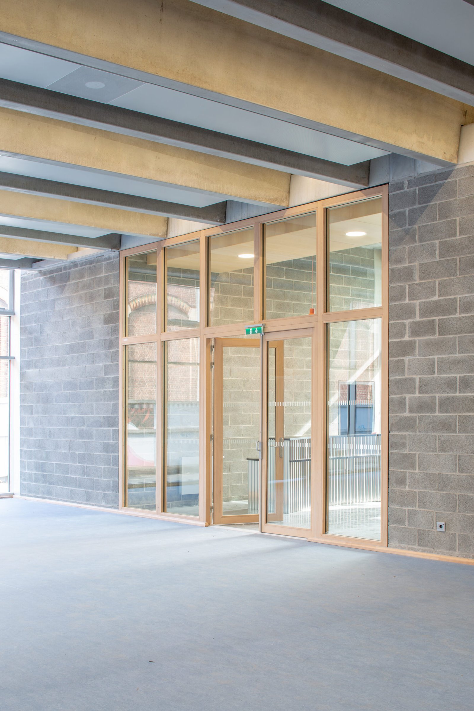 Salle multisports Saint-Sauveur - Lille Ensemble vitré et porte d'issue sous les poutres en béton du socle