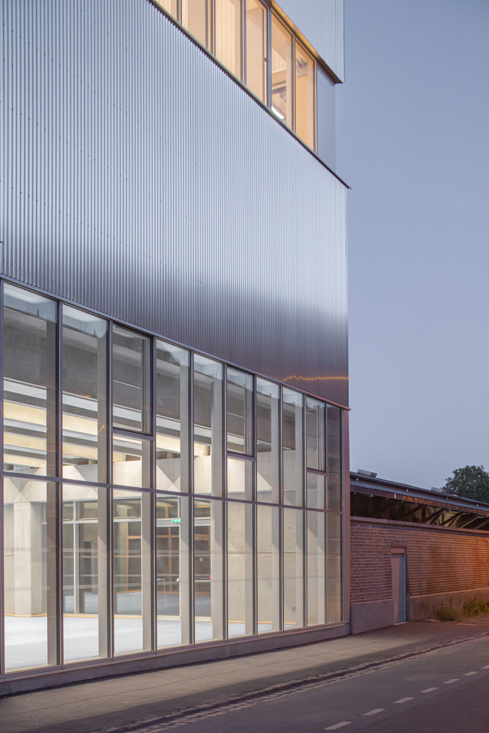 Salle multisports Saint-Sauveur - Lille Le socle vitré, sous le bardage en aluminium ondulé, au crépuscule