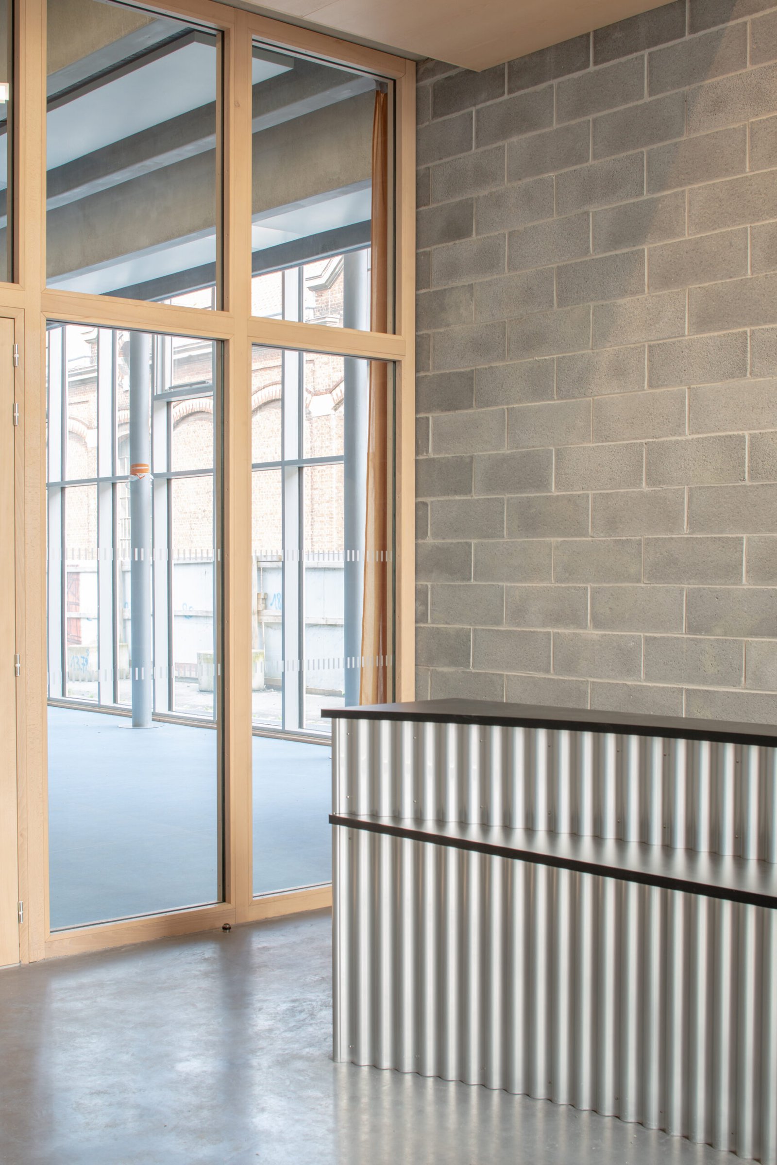 Salle multisports Saint-Sauveur - Lille Le hall d'accueil, ses menuiseries bois et son comptoir en tôle ondulée