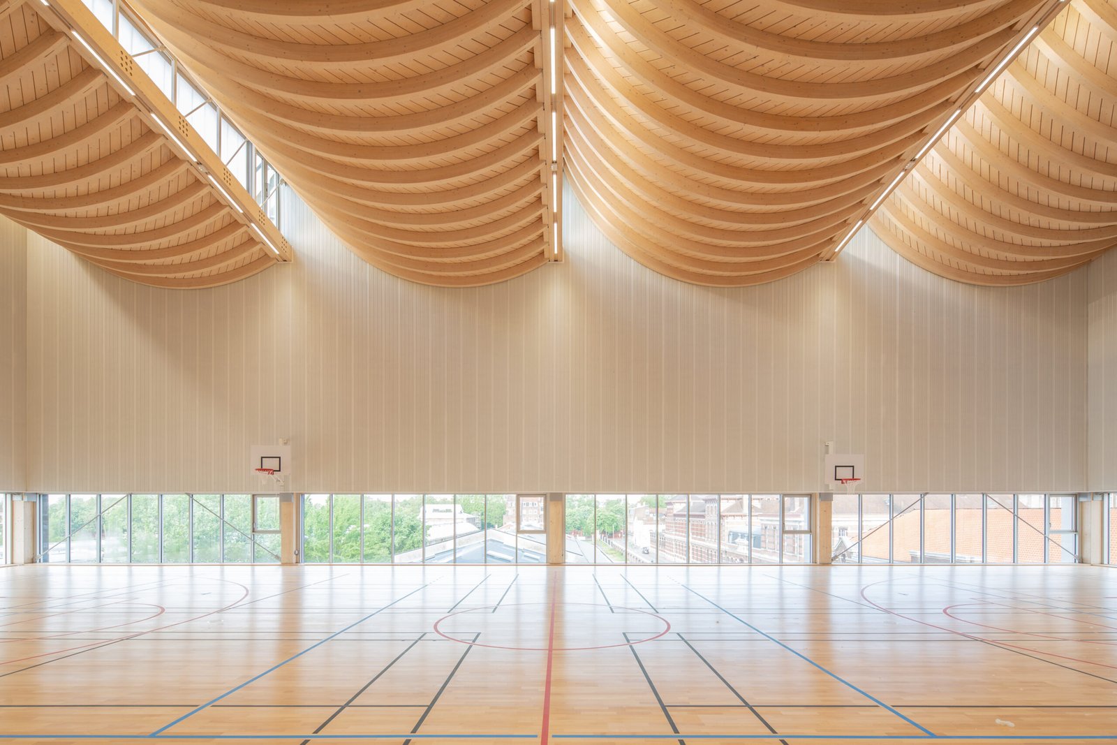 Salle multisports Saint-Sauveur - Lille La salle de basket sous la charpente en bois à coques courbes, avec vue sur le quartier
